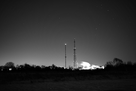 Communications towers and emitting smokestacks against the morning sky.